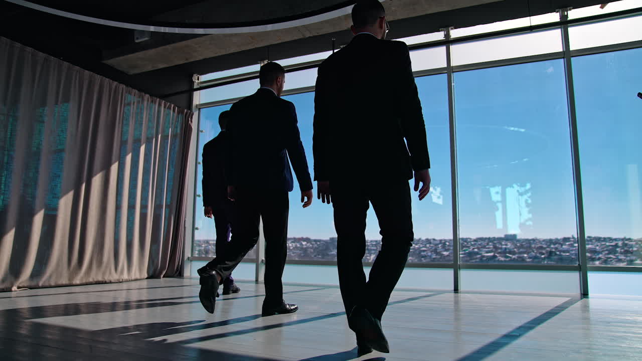Business people moving to the large office windows. Three men in suits walking to windows during break. Elegant entrepreneurs indoors. Slow motion.