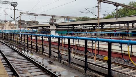 platform view at vadodara railway station, railway tracks with central waterline as train approaches under cloudy sky in gujarat, india.