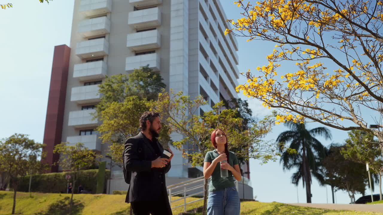 A man and woman observing and drinking under a yellow flowering tree in a city setting