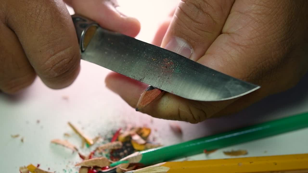 Opptak av hender som sakte spisser en blyant og noen fargeblyanter med en skarp kniv