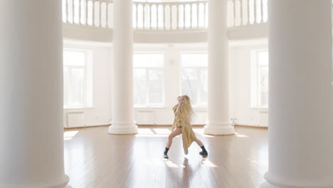 focused blonde woman in trench coat and boots training a contemporary dance in the middle of the studio