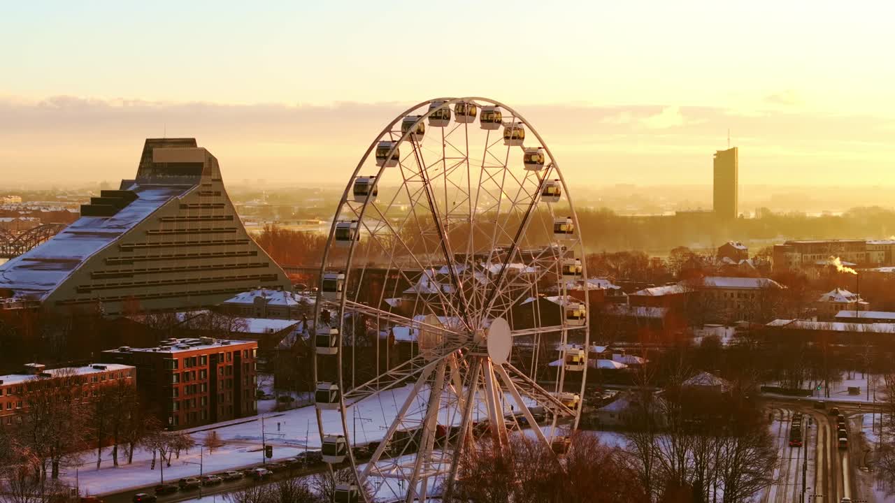 Warm sunrise light washes over snowy rooftops and ferris wheel in Riga Latvia