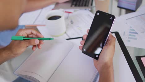 manos de un hombre afroamericano trabajando, sosteniendo un teléfono inteligente con espacio para copiar