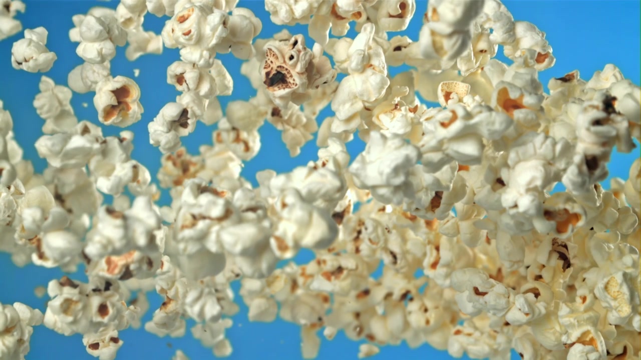 Popcorn che volano su e cadono giù al rallentatore su sfondo blu.