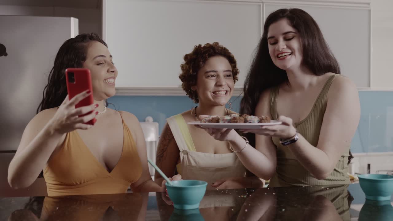 Happy friends taking a selfie in the kitchen with homemade desserts