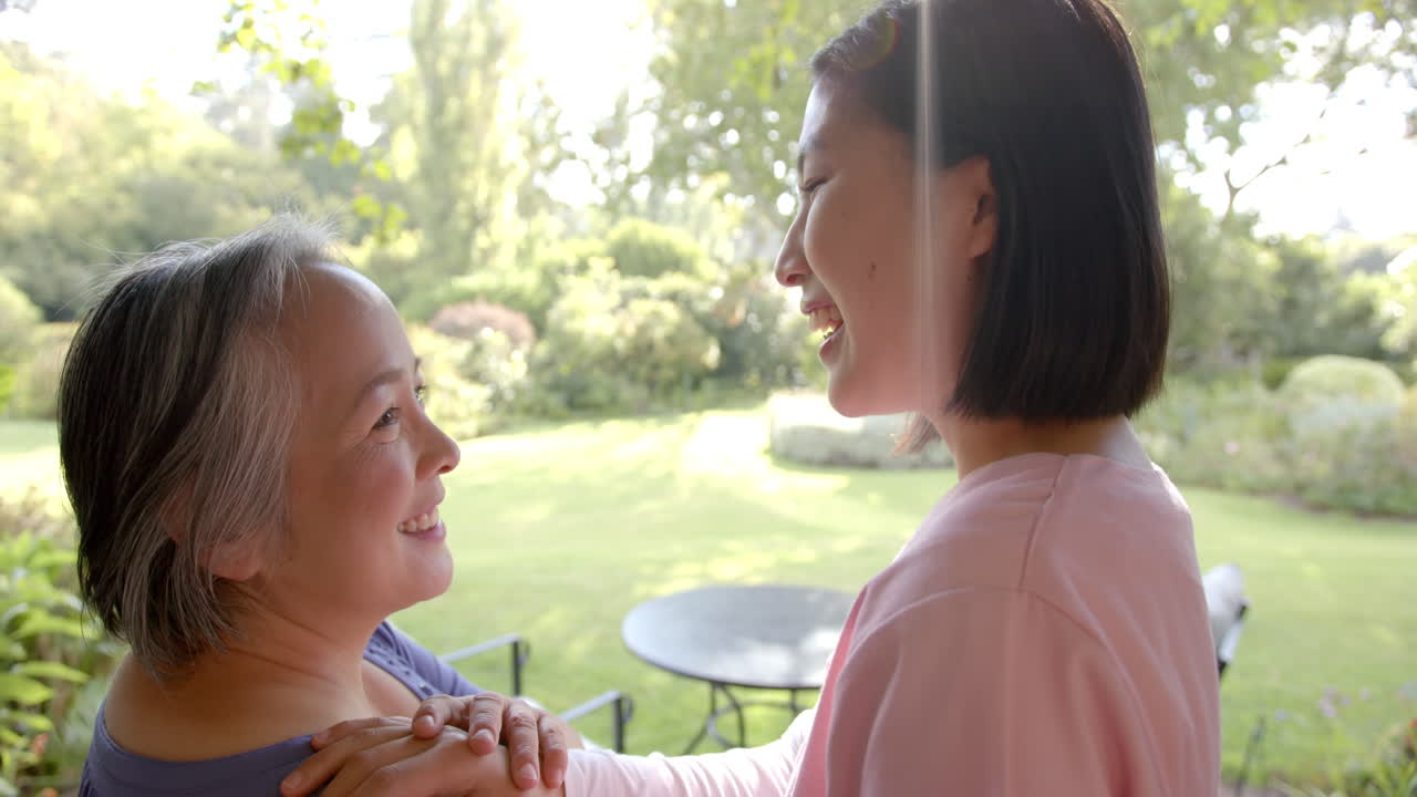 Smiling senior asian woman receiving physical therapy from caregiver in garden