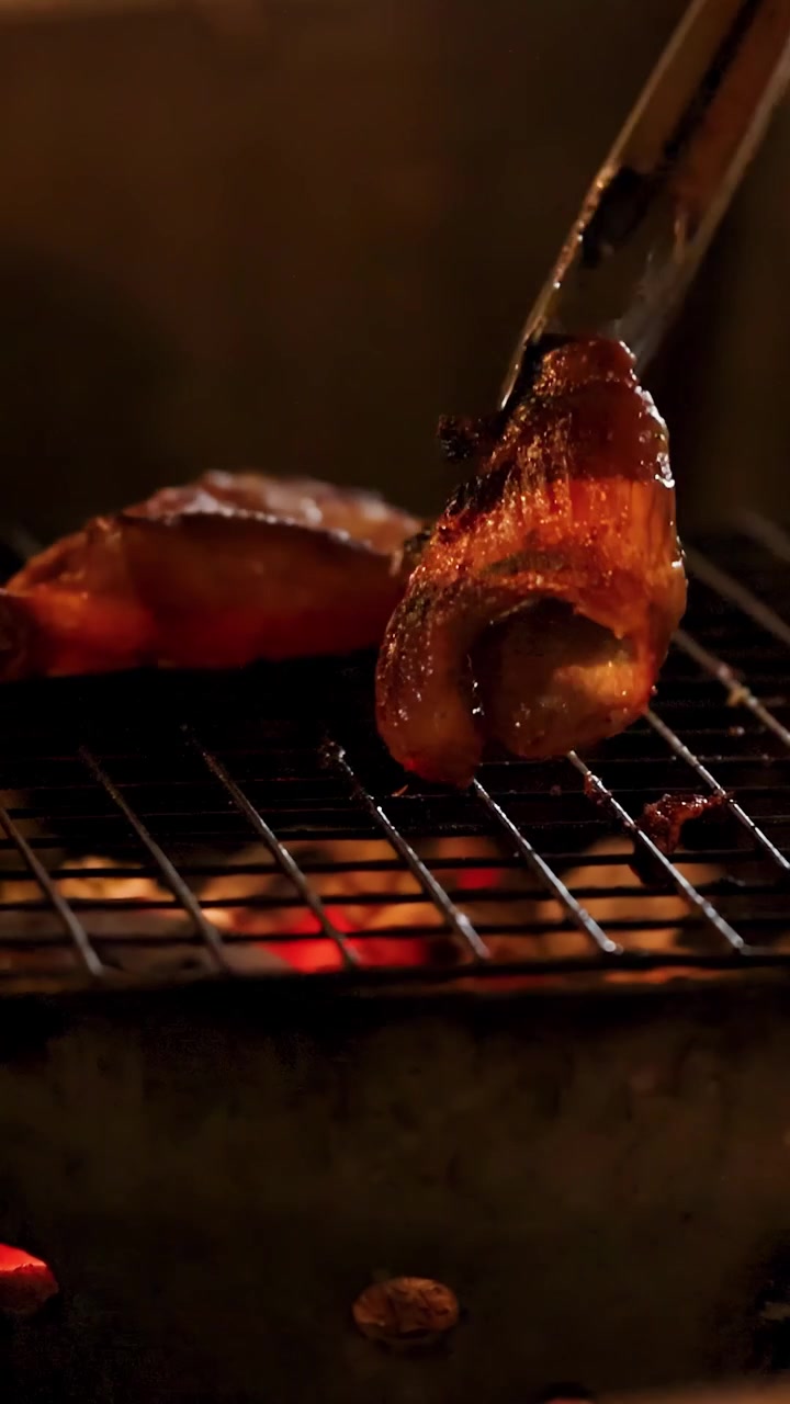Pinze di metallo girano pollo marinato su una griglia a carbone in un mercato di street food thailandese.