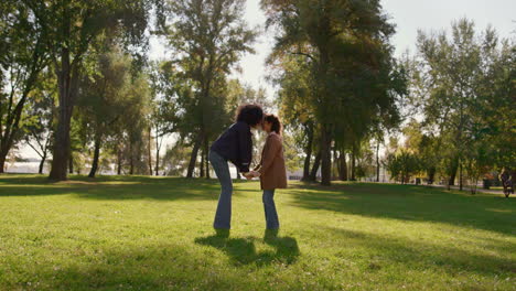Mother-holding-daughter-hands-gently-touching-noses-on-sunny-green-park-field.