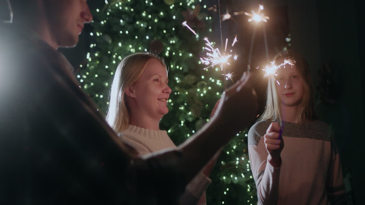 Una famiglia felice festeggia il nuovo anno all'albero di Natale, tenendo in mano stelle filanti accese