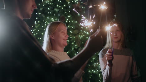 a happy family celebrates the new year at the christmas tree, holding burning sparklers