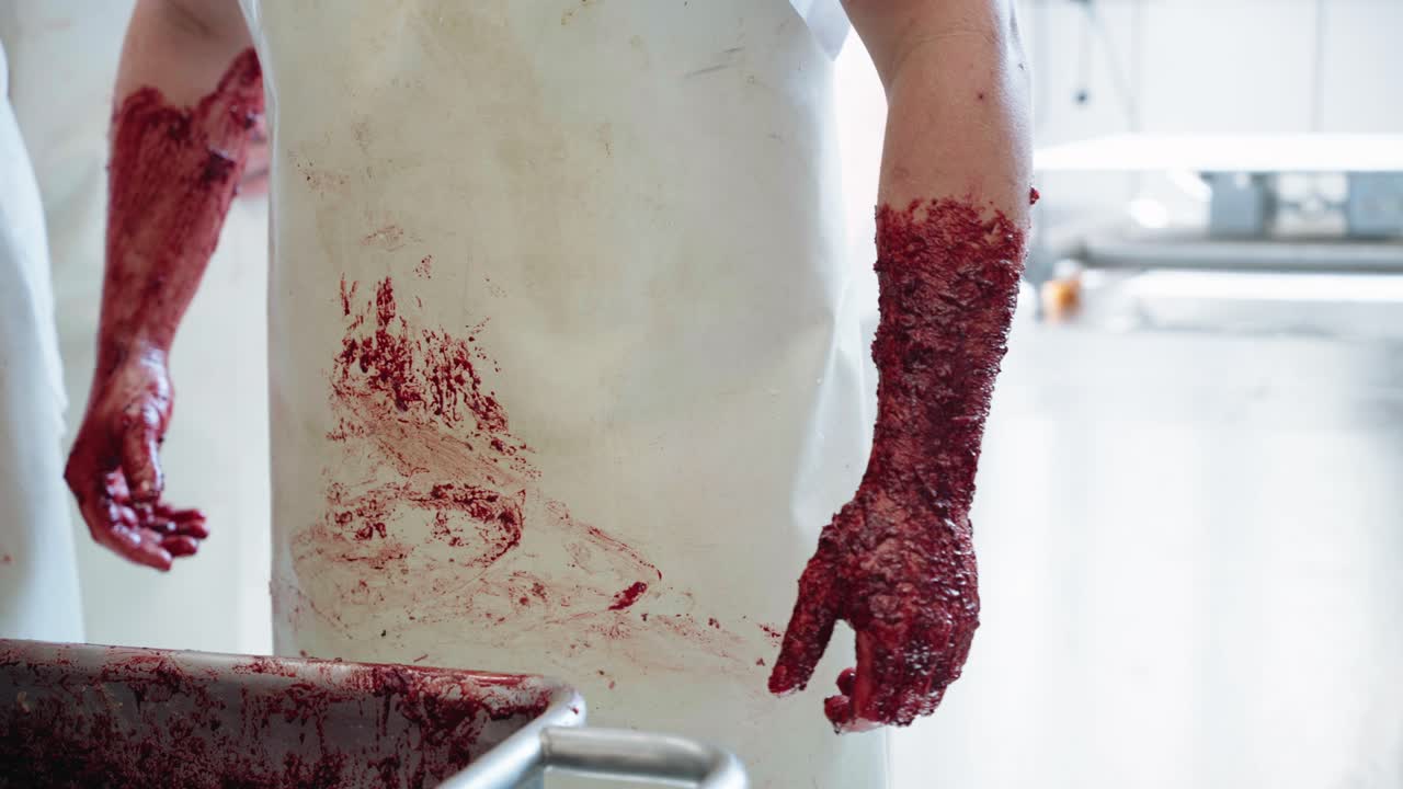 vista de las manos de los carniceros cubiertas de carne picada de sangre bratwurst junto al tanque de preparación