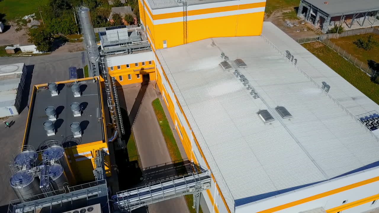 Yellow and white buildings of the industrial plant. Silver pipes among the premises of the factory. Circle drone footage.