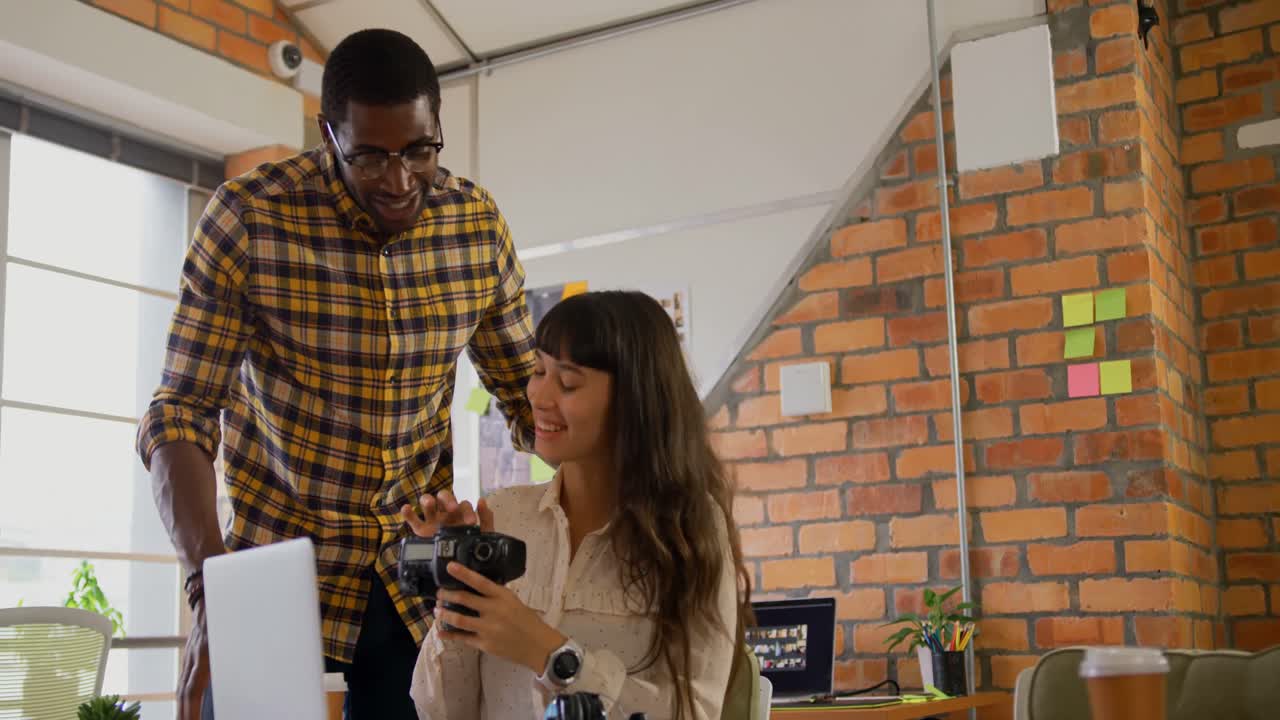 Graphic designers discussing over photographs on digital camera at desk 4k