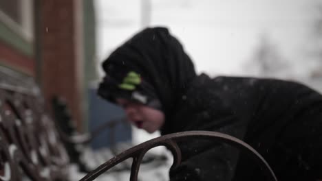 Young-boy-wearing-a-coat-playing-in-the-snow-outside-on-a-cold,-winter-day-in-December-with-a-snow-covered-bench-during-Christmas-break-in-a-small-town-in-the-midwest