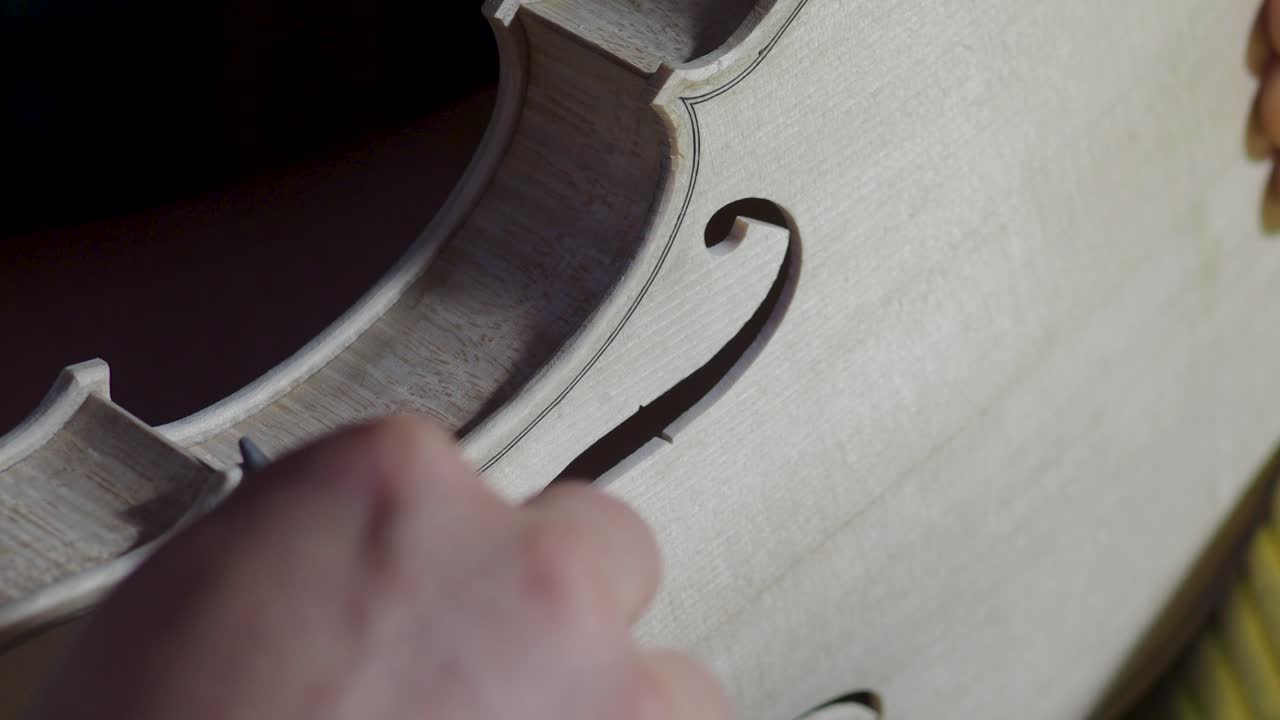 macro primer plano de artesano luthier fabricante de trabajo en nuevo clásico hecho a mano violín crudo borde liso en la cintura y raspado púrpura en el banco de trabajo del taller en cremona italia video 4k