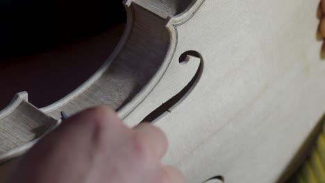 macro close up of artisan luthier maker work on new classic handmade raw violin smooth edge in waist and purfling rasp in workbench of workshop in cremona italy 4k video