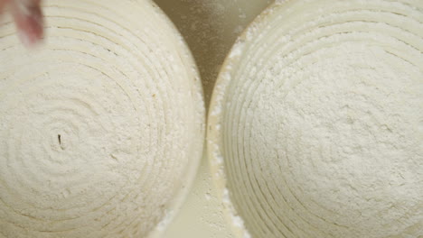 top view of a baker dusting two proofing baskets with some organic flour