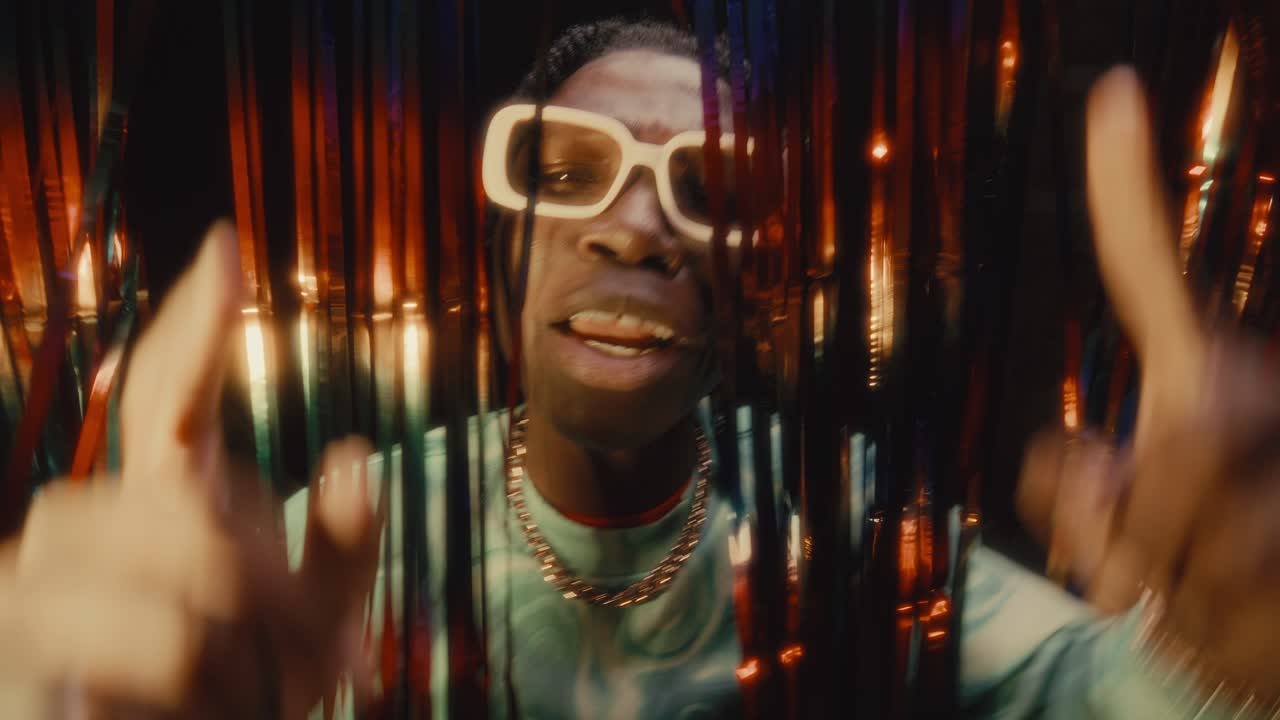 Black Hip-Hop Artist Rapping to Camera behind Tinsel Curtains in Nightclub