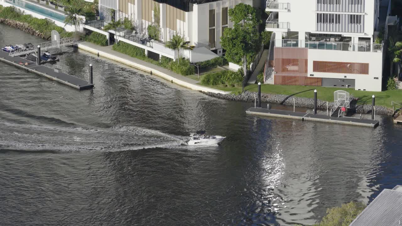 Aerial view of a boat navigating a canal in Gold Coast, Australia. Sunny day, modern buildings, and lush greenery visible