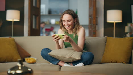 Aufgeregt-Lachende-Frau-Mit-Smartphone-Auf-Der-Couch-Zu-Hause.-Glückliche-Dame-Spielt-Mit-Handy