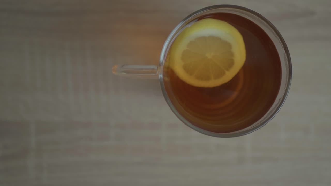 A cup of lemon tea - with a slice of citrus on it swirling in a clockwise motion - close up