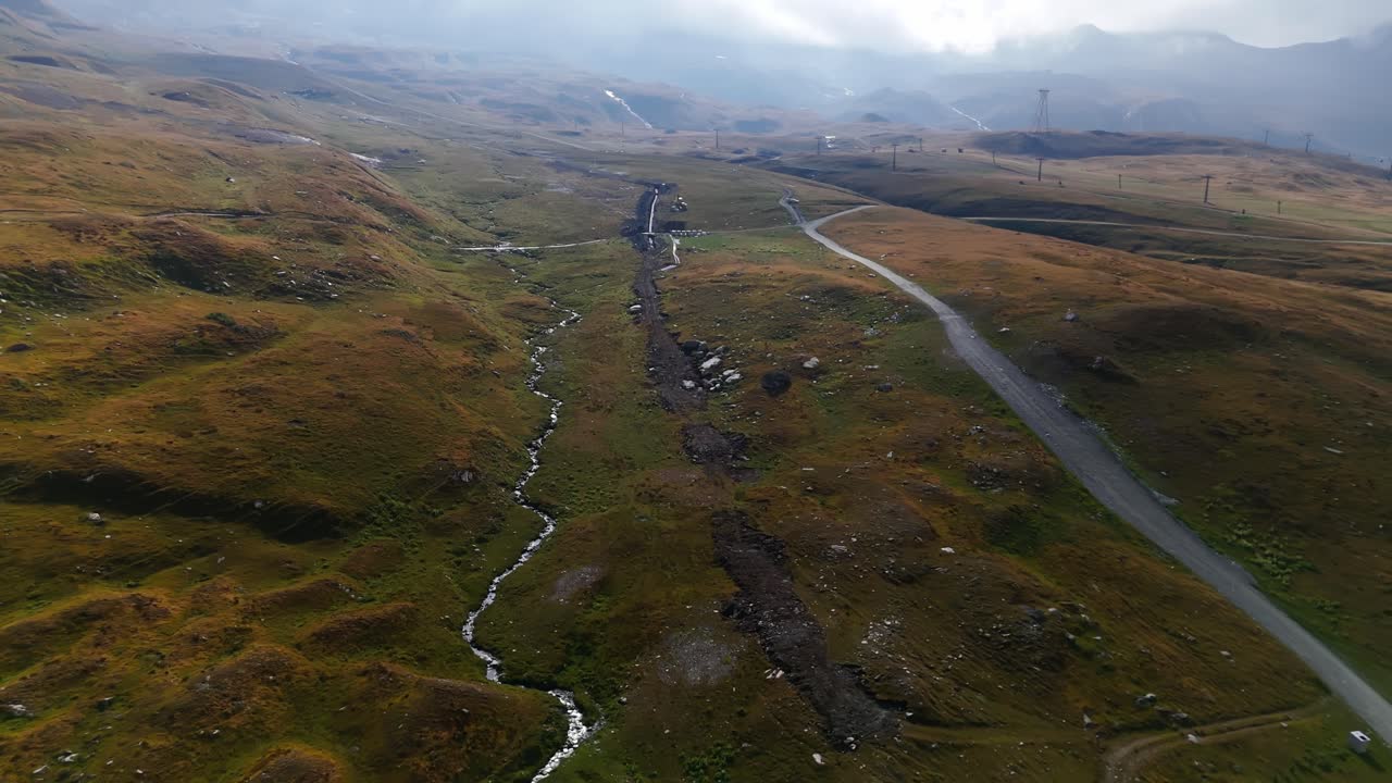 Pulling back aerial shot revealing a stunning misty landscape with a winding road in Cervinia, Italy, Aosta Valley, showcasing atmospheric alpine scenery