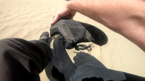 cámara lenta - la persona se quita el zapato en el desierto y vacía la arena del zapato