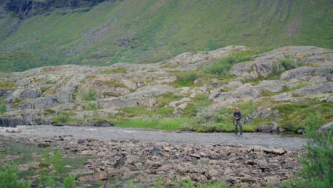man fly fishing in stream by green mountains in sweden, wide view