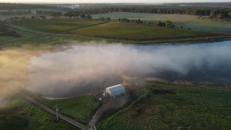 mystic fog flying over australian countryside farm fields and lake during sunrise in the morning