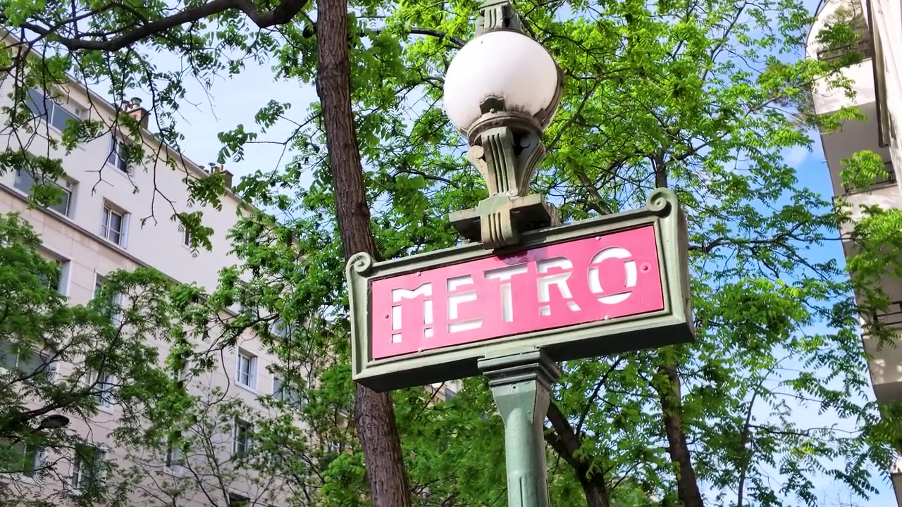 Inquadratura dal basso di un cartello rosso della metropolitana di Parigi contro alberi verdi ed edifici.