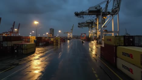 a nighttime view of a quiet shipping port with cranes and containers under low lighting, reflecting on wet pavement, evoking a calm yet industrious atmosphere