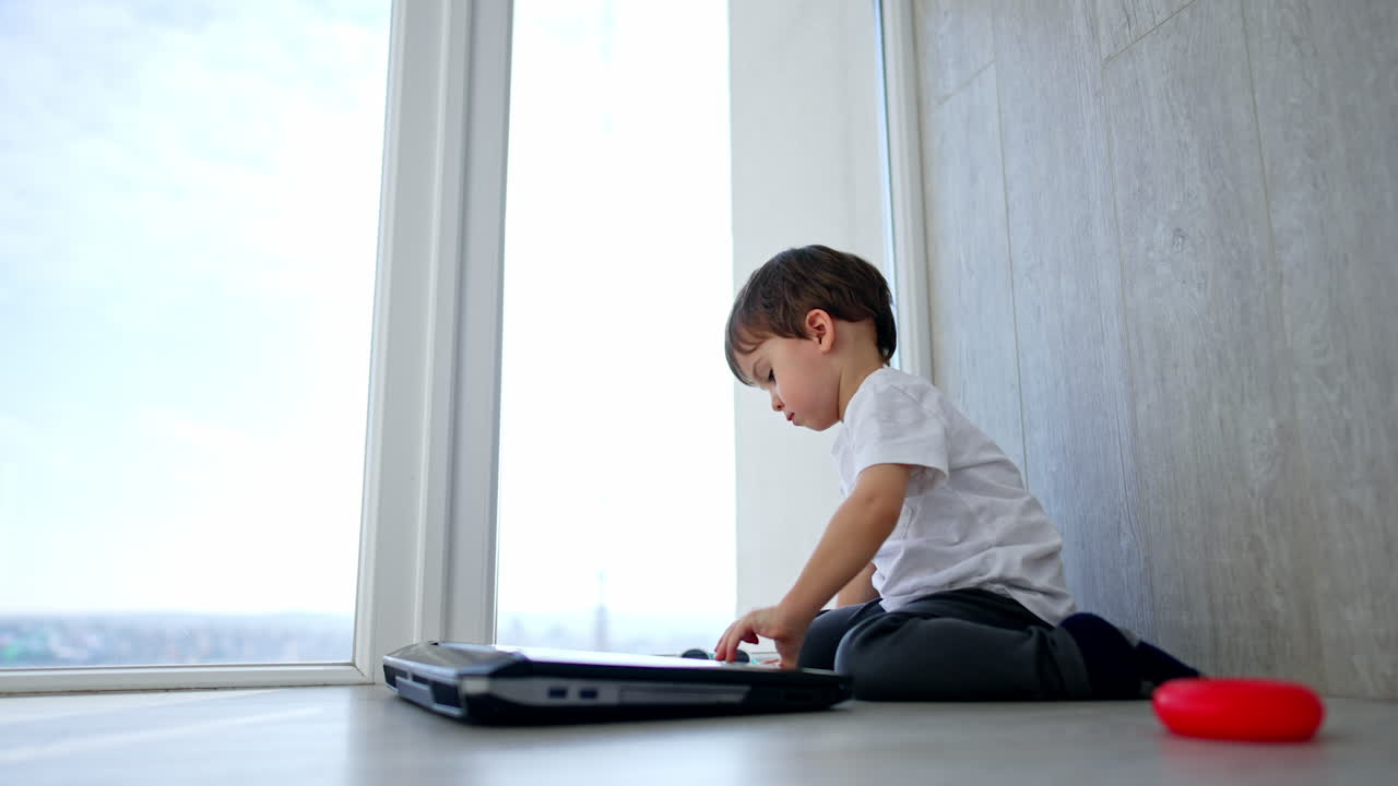 A little boy is sitting on the floor and playing a laptop.
