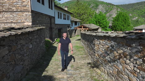 young man walking along the stone walls in traditional village of kovachevitsa, bulgaria. - pullback shot