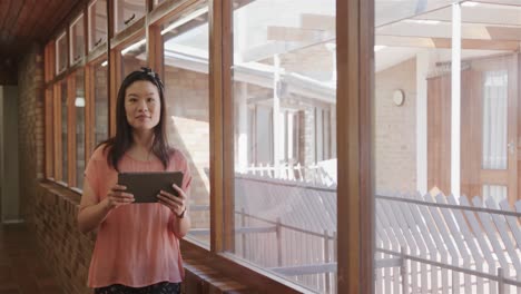 Glückliche-Asiatische-Lehrerin-Mit-Tablet-Im-Schulkorridor-Der-Grundschule,-Kopierraum