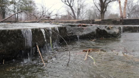 Slow-motion-shot-of-a-small-waterfall-cascading-over-a-stone-ledge-during-winter