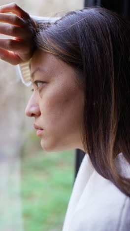 vertical video close up of stressed or anxious woman suffering with depression anxiety loneliness or agoraphobia leaning against window at home 3