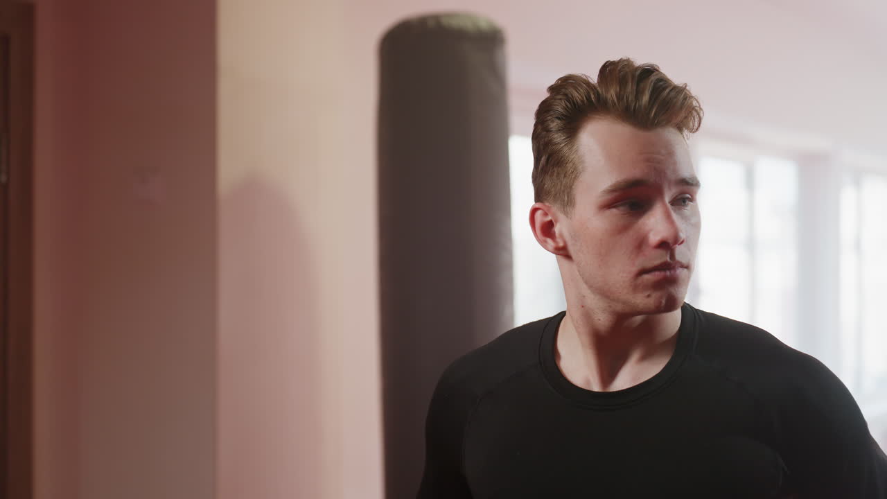 Man in gym environment wearing a black long sleeve shirt over head, revealing toned torso and tattoo on neck, preparing for workout session with intensity, focus, discipline, determination