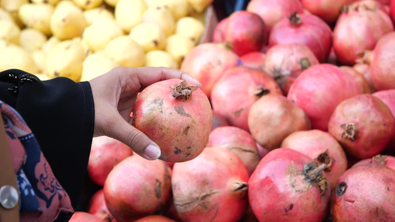 la mano de una mujer seleccionando una granada en un mercado de frutas