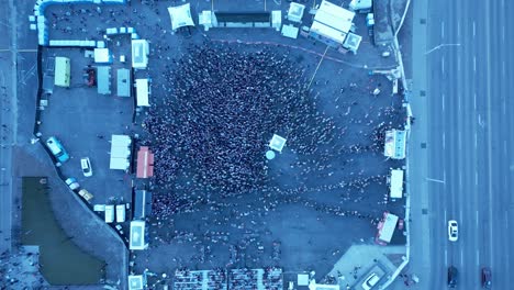 mosh pit fans gather to watch stage performance surrounded by food trucks mass line ups with a big screen tv as white beach ball gets tossed around in a downtown city birds eye top view next to road