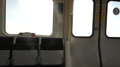 Inside-View-Of-Empty-Folded-Up-Seats-On-Metropolitan-Line-Train-Carriage-With-Bright-Sunshine-And-Sun-Flares-Through-Carriage-Windows