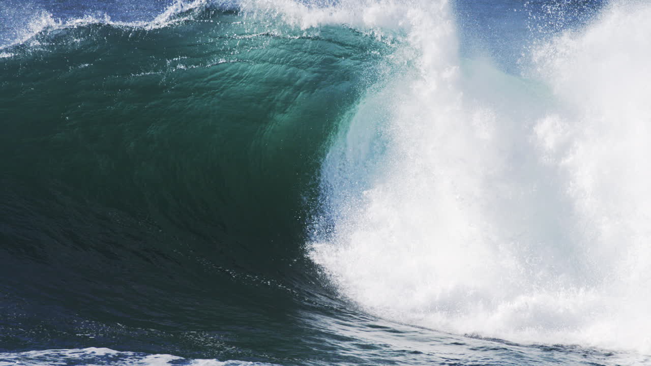 Foamy crashing wave rolls in under sunlight with mist and vivid surface ripples