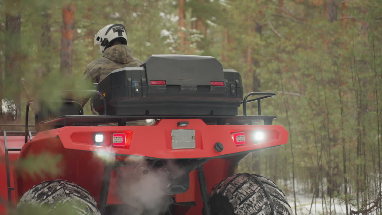Primo piano posteriore di un quad rosso in foresta innevata che mostra vapore dallo scarico, fanale posteriore illuminato e pneumatici robusti, pilota con casco bianco che controlla il percorso, baule portaoggetti, atmosfera tesa e avventurosa, fuoristrada estremo.
