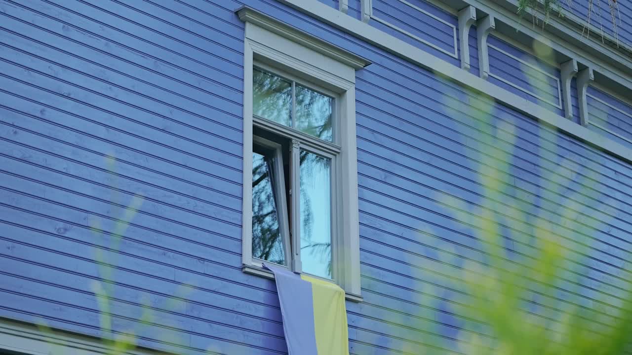 Worn yellow and blue Ukrainian flag displayed on window of house in Latvia