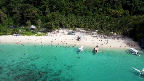 vista aérea: barcos de estilo catamarán filipino que atraviesan en primer plano la playa tropical de siete comandos , turistas nadando en aguas claras de color turquesa en arena blanca
