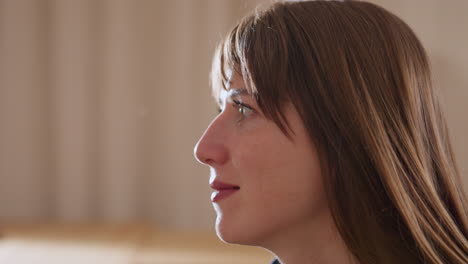 side view of emotional coach with long brown hair smiling gently while seated in bright restorative room, expressing compassion and attentiveness during thoughtful therapeutic conversation