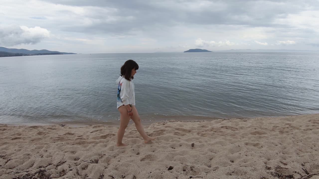 부분적으로 흐린 날 그리스 해변에서 맨발로 걷는 젊은 브루네트 여성의 트럭 이동