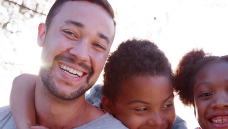 Parents-Giving-Children-Piggybacks-On-Walk-Through-Park-With-Grandparents