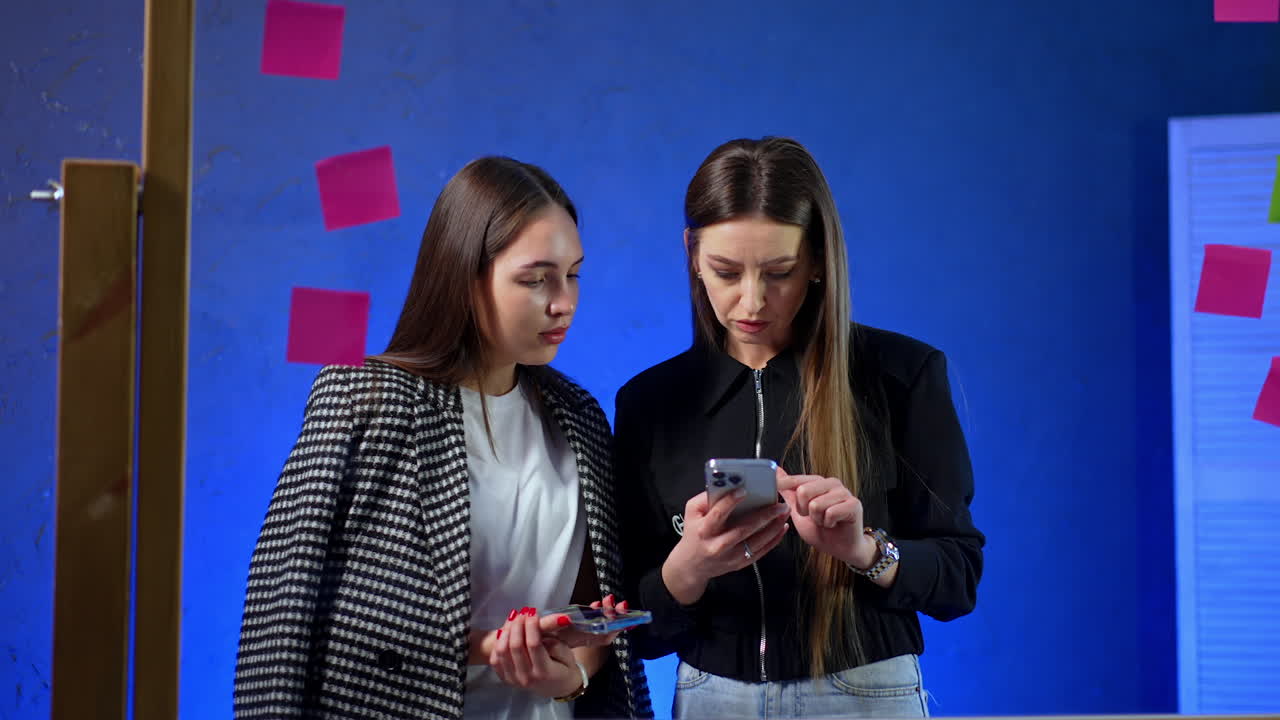 Discussion about ideas during a meeting. Two women are engaged in a focused discussion while looking at a smartphone in a creative workspace with bright colors