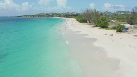 Aerial-tilt-up-view-shot-tourist-have-fun-relax-on-caribbean-coast-white-sand-beach-in-Antigua-and-Bermuda