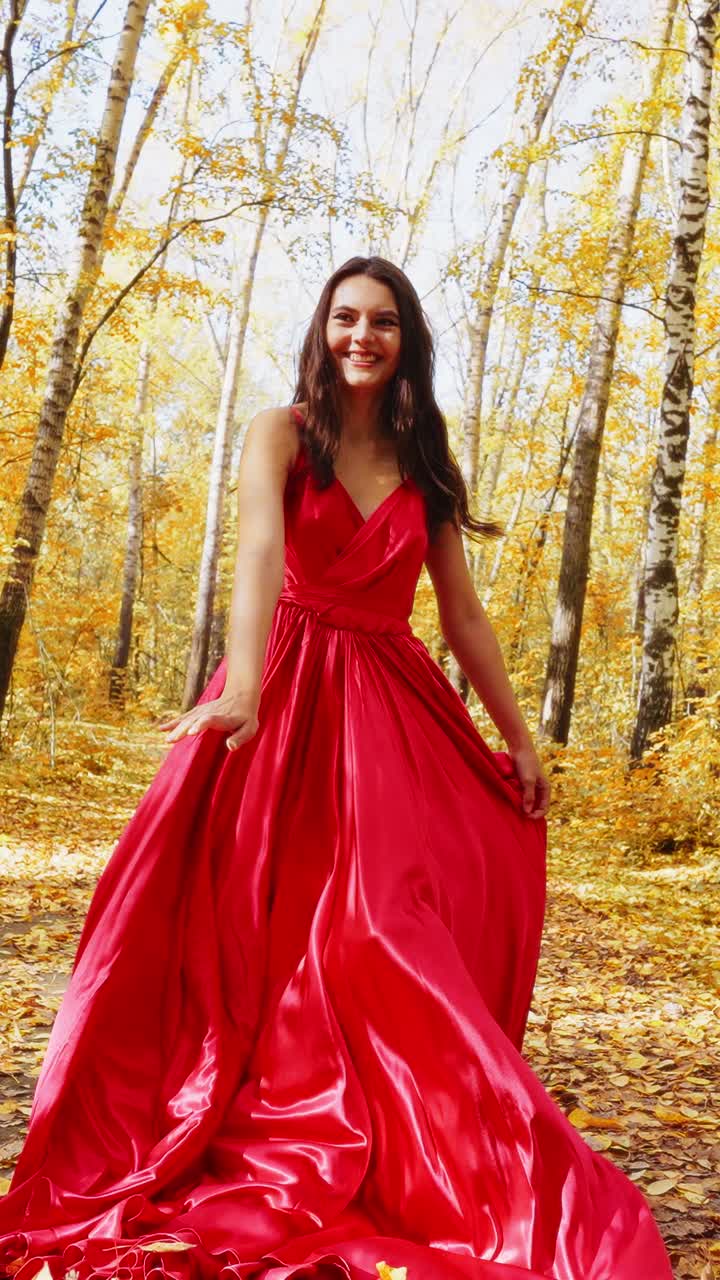 A Woman in a Stunning Red Dress Radiates Joy Among Vibrant Autumn Leaves, Capturing the Essence of Nature's Beauty and Elegance in a Picturesque Forest Setting